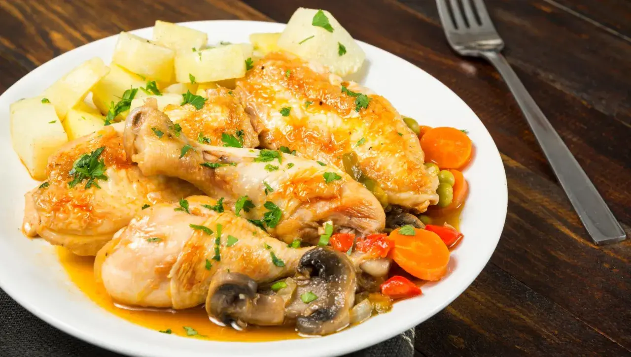 Sabroso pollo a la pepitoria con patatas, zanahorias, guisantes y champiñones, todo espolvoreado con perejil fresco.