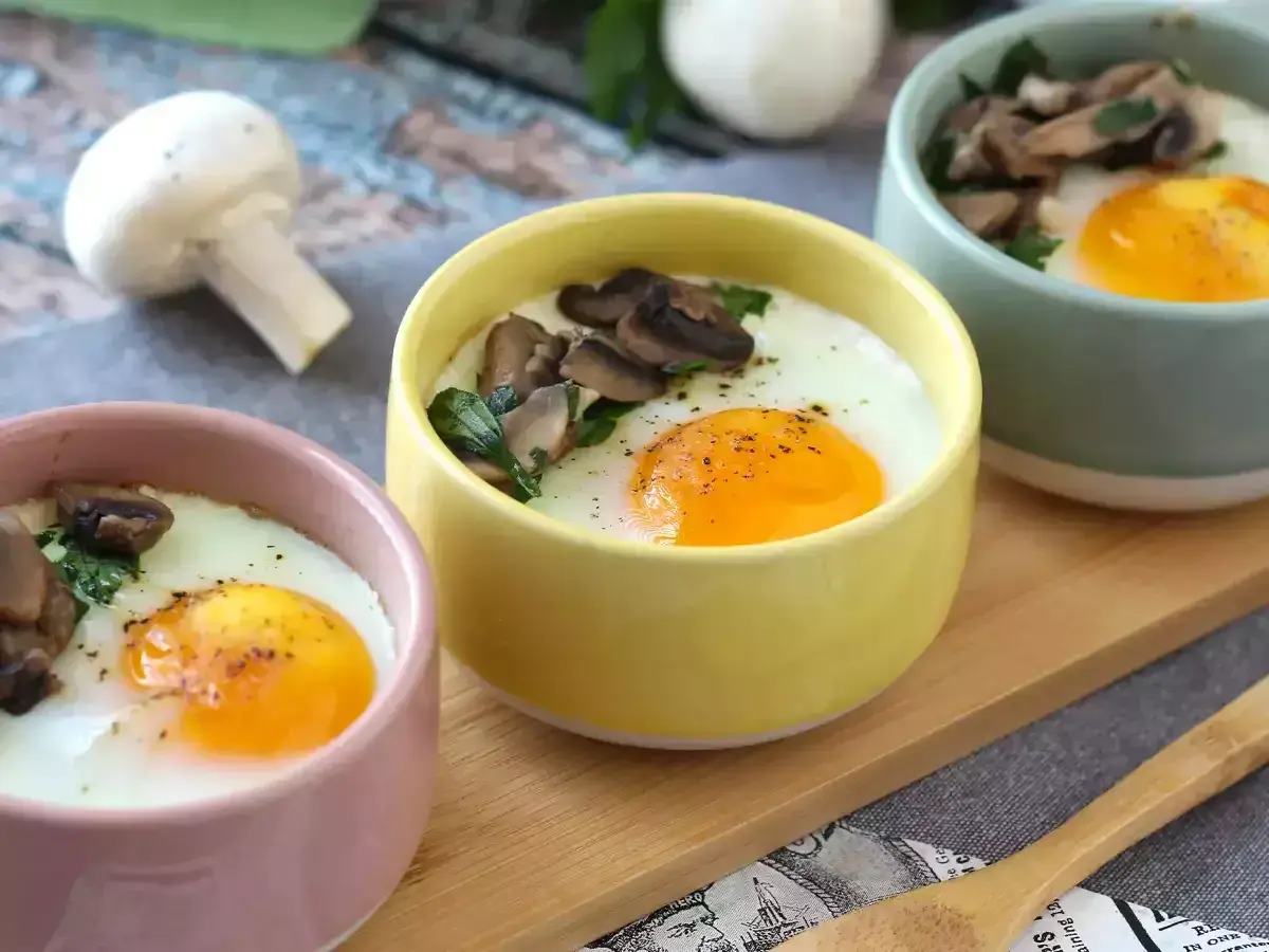 Deliciosos huevos al horno con champiñones y perejil, servidos en coloridas tazas. Un desayuno perfecto.
