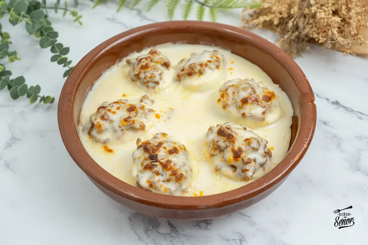 Huevos rellenos gratinados con bechamel y queso, servidos en una cazuela de barro.