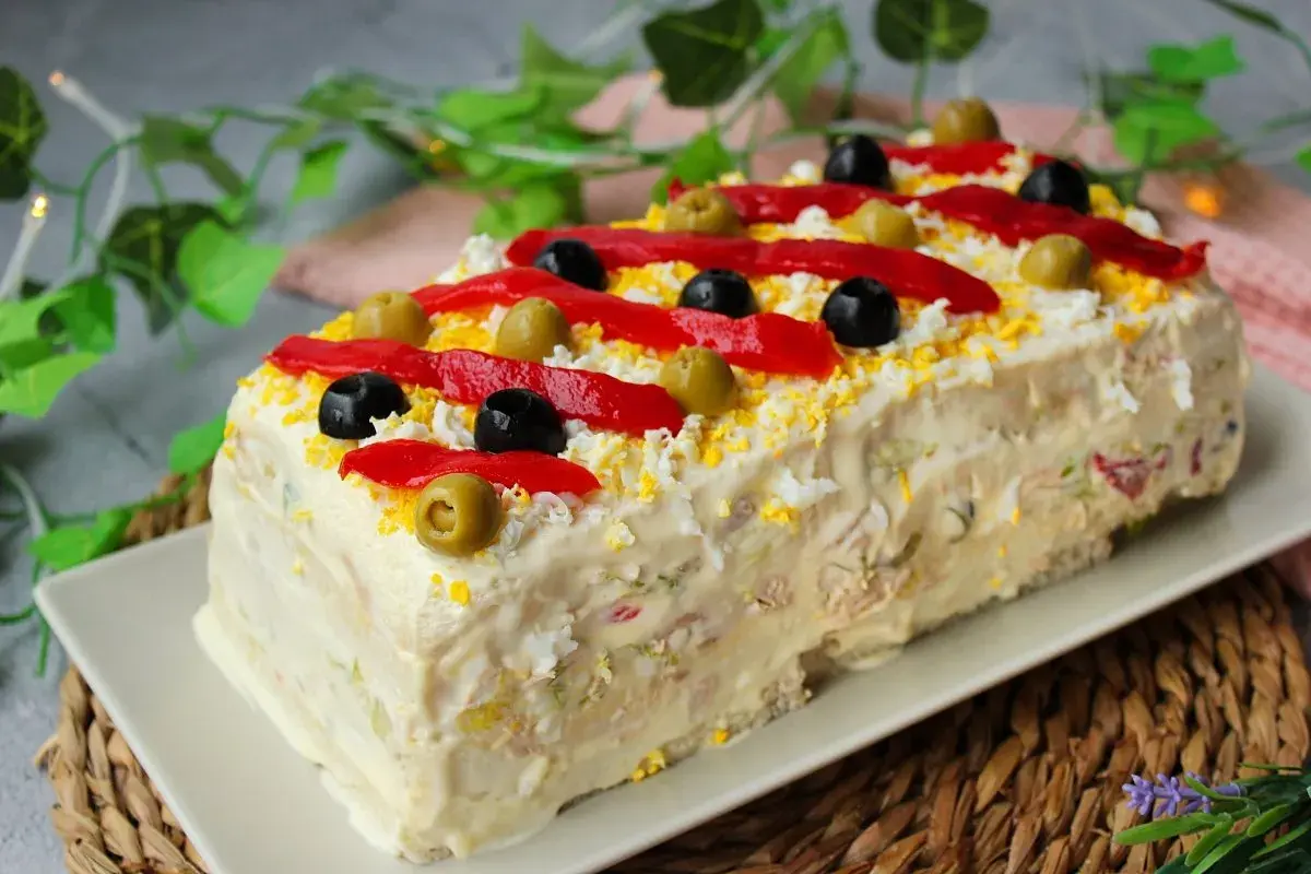 Pastel de atún decorado con pimientos rojos, aceitunas negras y verdes, y huevo rallado. ¡Una delicia para compartir!
