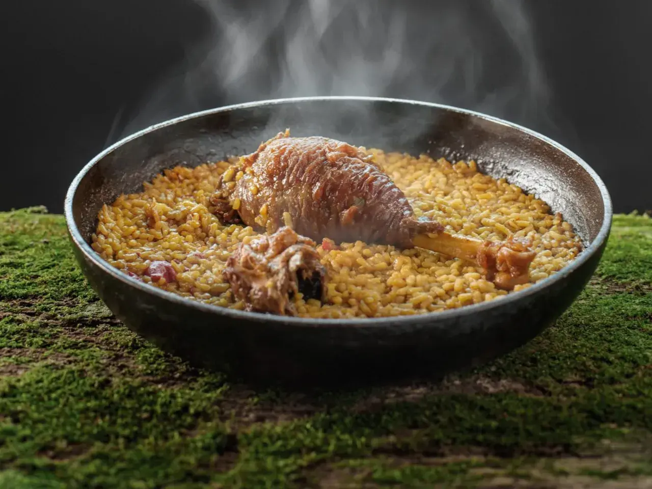 Arroz meloso con pitu de caleya, humeante y servido en paellera sobre un lecho de musgo.