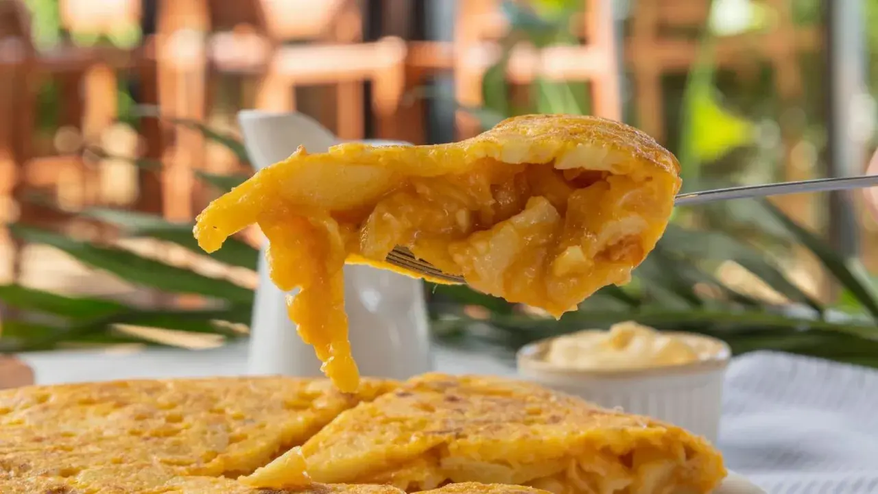 Un tenedor levanta un trozo jugoso de pincho de tortilla, mostrando su interior de patatas y huevo.