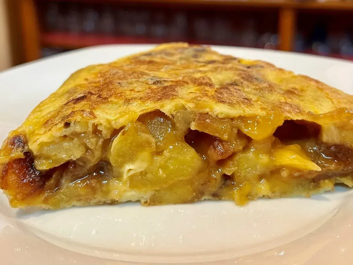 Un trozo jugoso de tortilla de patatas, con patatas tiernas y huevo dorado, servido en un plato blanco.