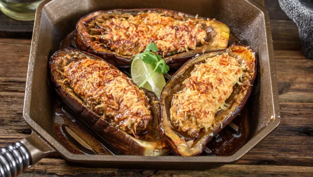 Berenjenas rellenas airfryer doradas y gratinadas, servidas en una sartén de hierro fundido con una rodaja de lima.