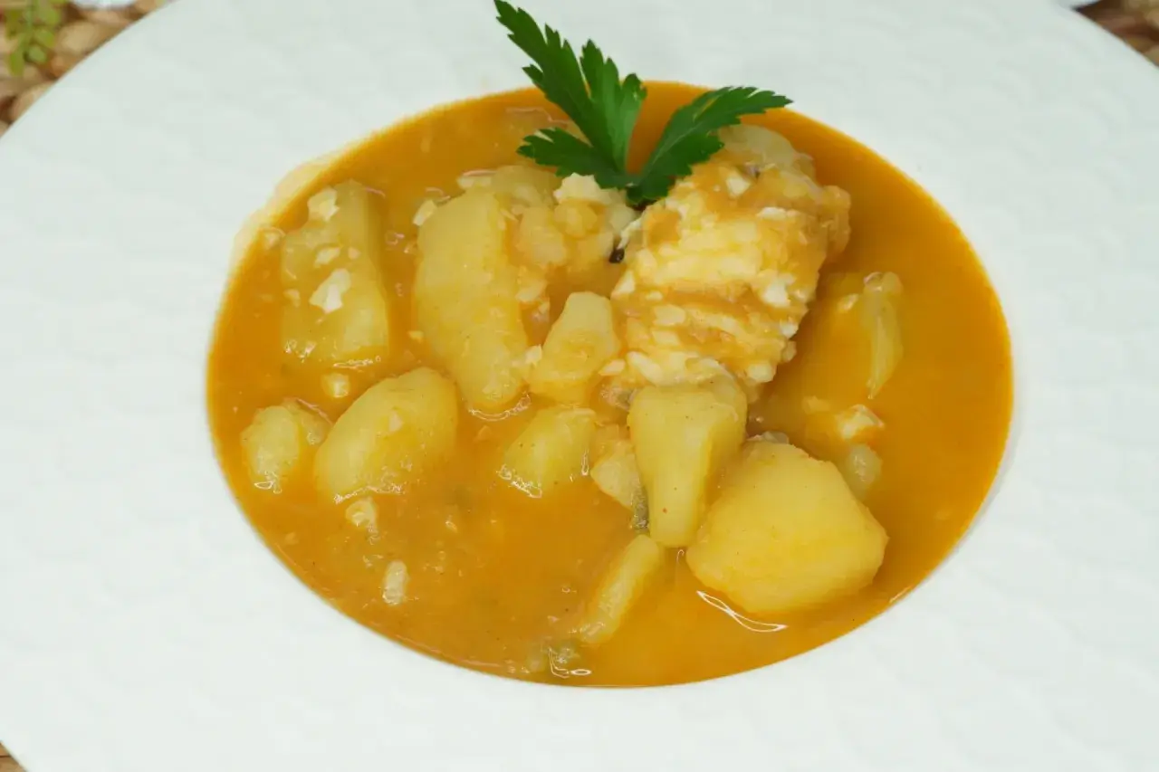 Un plato de patatas con bacalao en una salsa naranja, decorado con perejil.