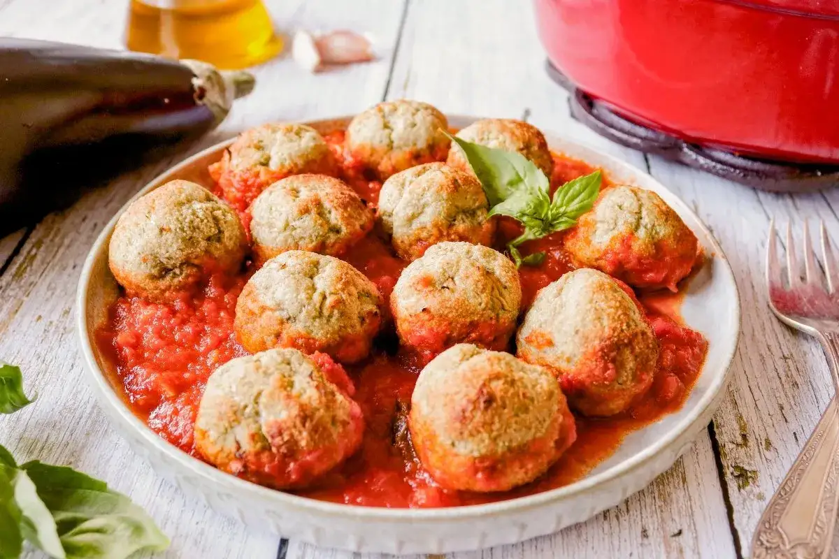 Albondigas de berenjenas caseras, servidas en una salsa de tomate vibrante con hojas de albahaca fresca.