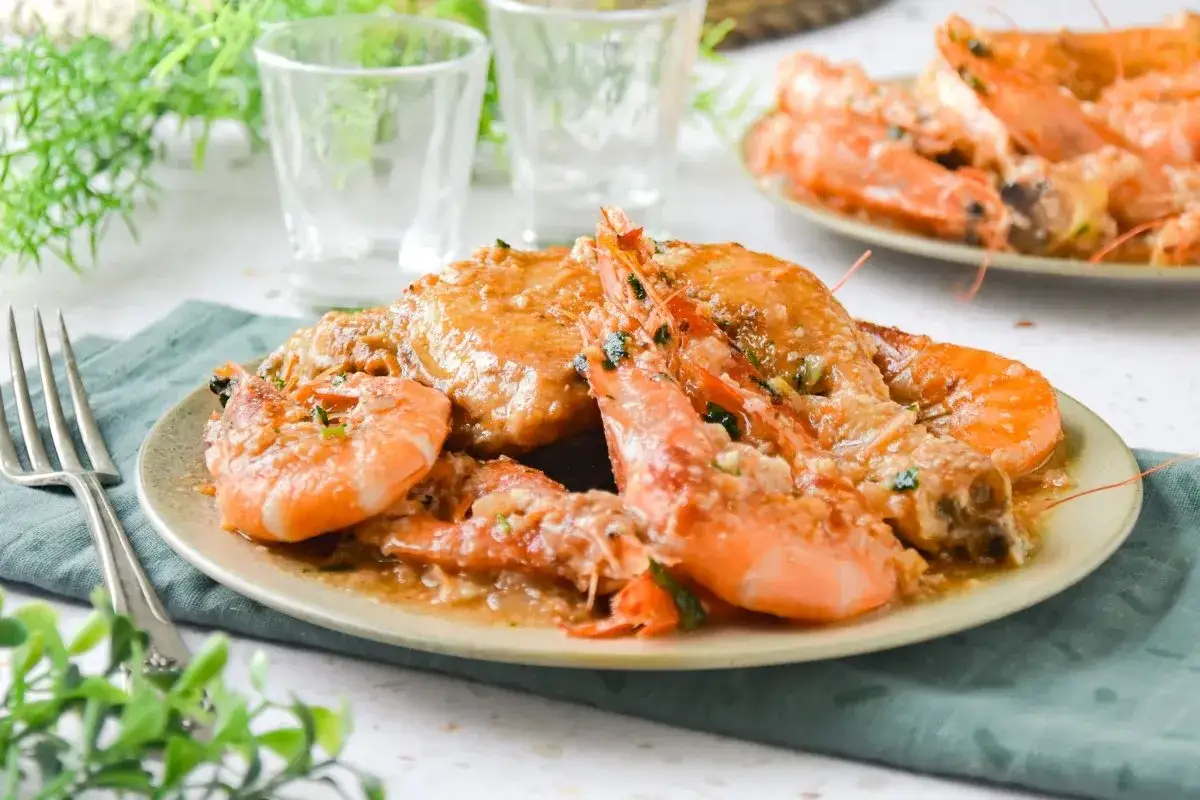 Plato de pollo con gambas en salsa, decorado con perejil picado. Se ve delicioso y listo para servir.