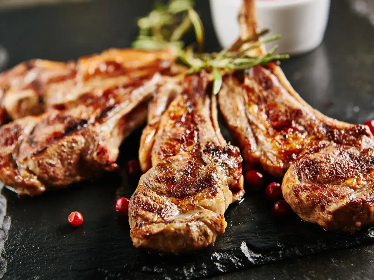 Chuletillas al sarmiento, jugosas y doradas, servidas con bayas rojas y romero sobre pizarra.