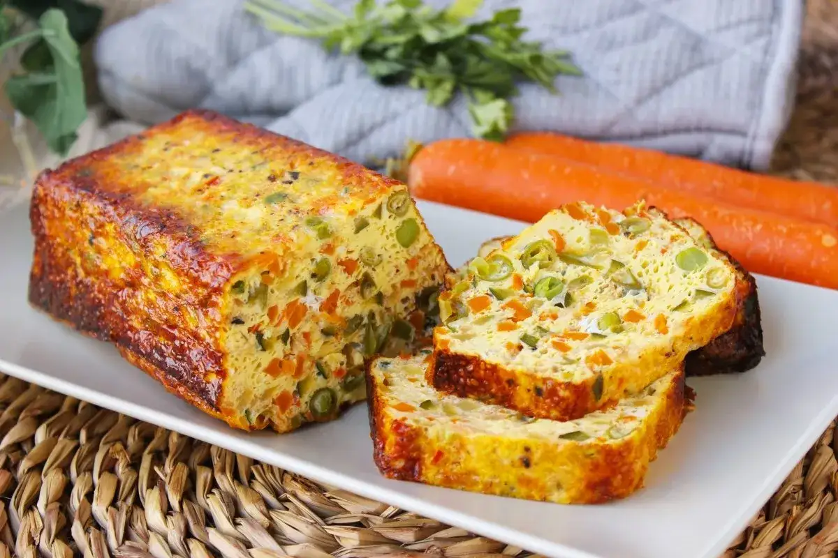 Pastel de verduras casero, con trozos de zanahoria y guisantes, servido en una bandeja blanca.