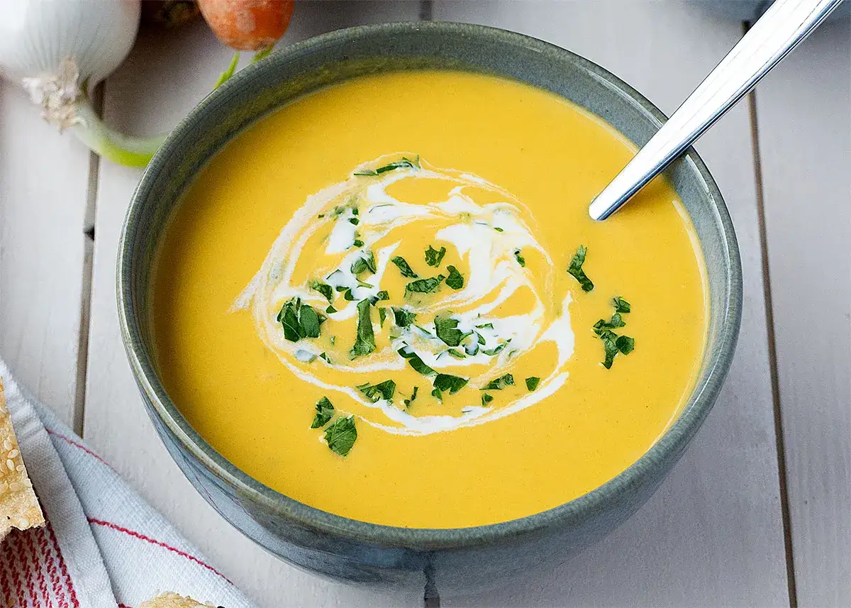 Crema de zanahoria, perfecta para tus recetas con zanahoria. Servida en un cuenco con un remolino de nata y perejil picado.