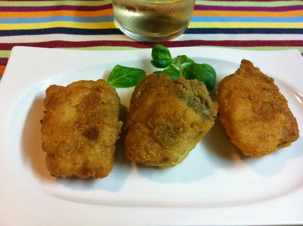 Tres trozos de merluza en adobo, dorados y crujientes, servidos en plato blanco con hojas verdes.