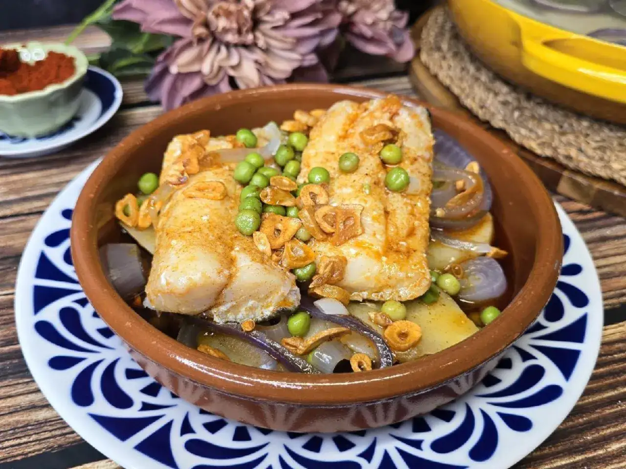 Bacalao a la gallega con patatas, cebolla, guisantes y ajo crujiente en cazuela de barro.