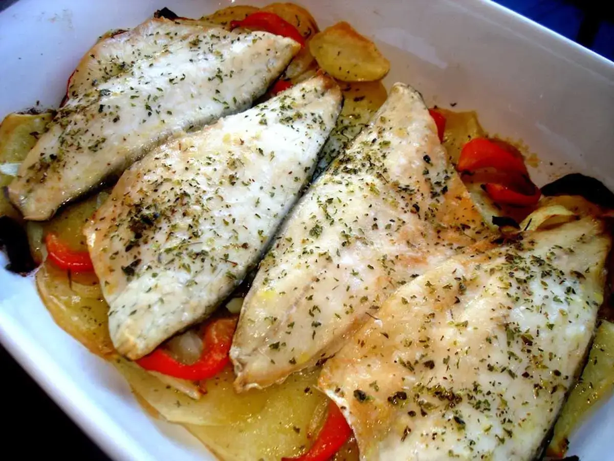 Filetes de lubina al horno con patatas y pimientos rojos, espolvoreados con hierbas aromáticas.