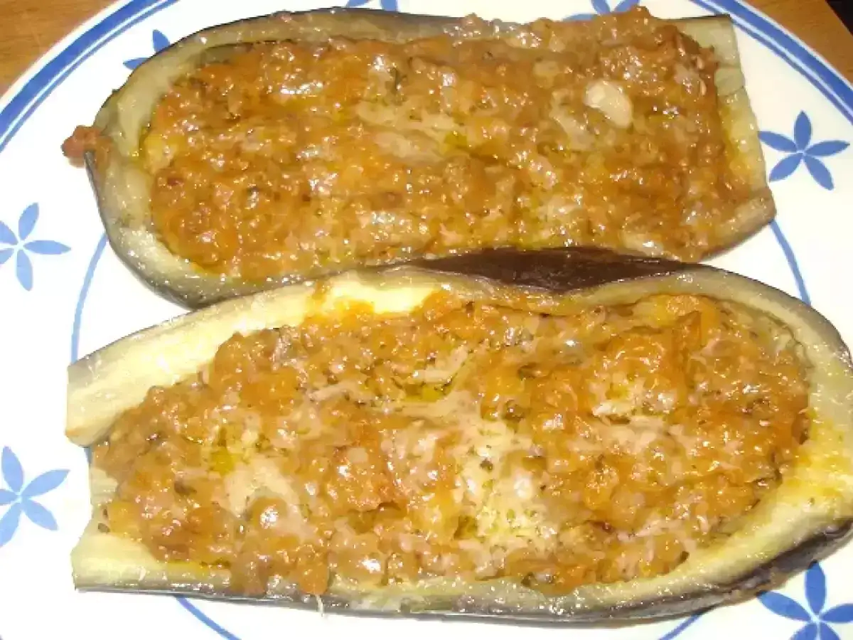 Dos mitades de berenjenas rellenas de verduras, horneadas y doradas, servidas en un plato con borde azul.