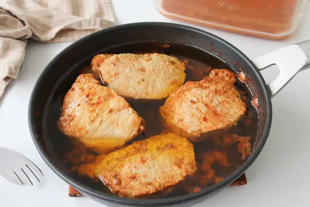 Cuatro trozos de lomo de orza se cocinan en una sartén con un líquido oscuro y especiado.