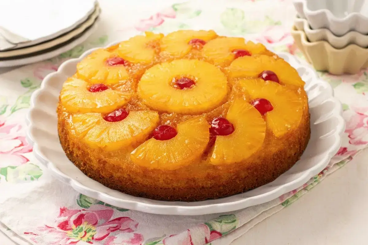 Tarta de pi&ntilde;a dorada con rodajas de pi&ntilde;a y cerezas rojas en la parte superior, lista para disfrutar.