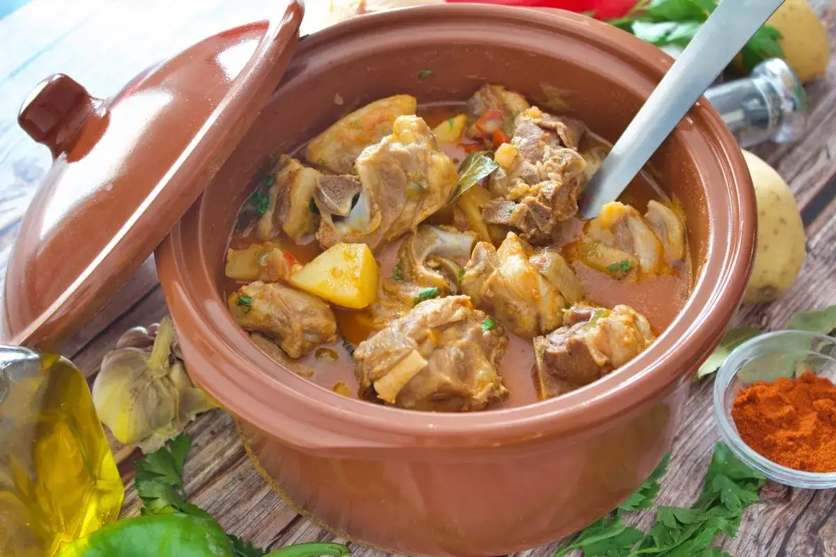 Caldereta de cordero humeante en cazuela de barro, con patatas y hierbas. Un plato tradicional listo para servir.