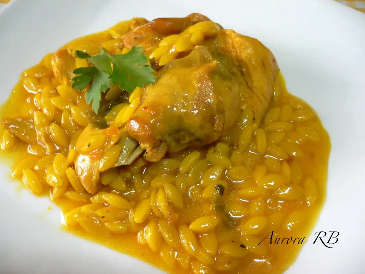 Gurullos con conejo, un plato tradicional con trozos de conejo en una salsa amarilla y arroz en forma de grageas, decorado con perejil.