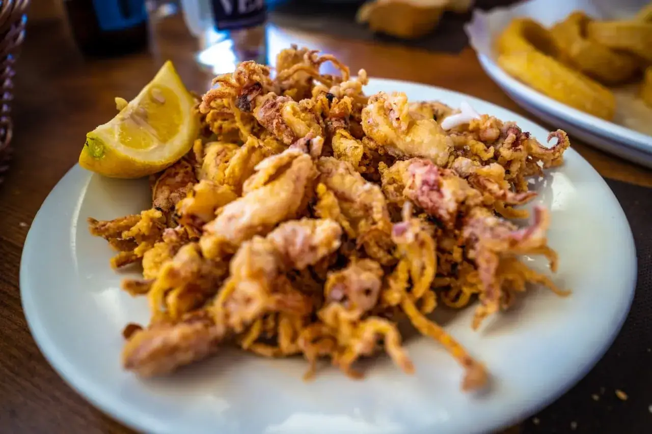 Plato de puntillas de calamar crujientes y doradas, servido con una rodaja de lim&oacute;n fresco.