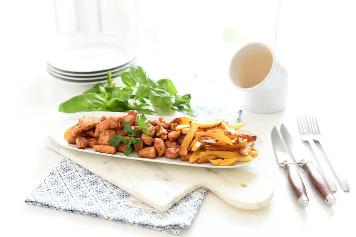 Sabrosa zorza con patatas fritas, servida en una bandeja ovalada con perejil fresco y una guarnici&oacute;n de albahaca.