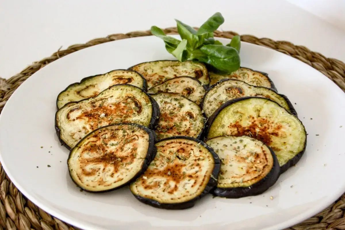 Rodajas de berenjena a la plancha, sazonadas con hierbas y especias, servidas en un plato blanco.