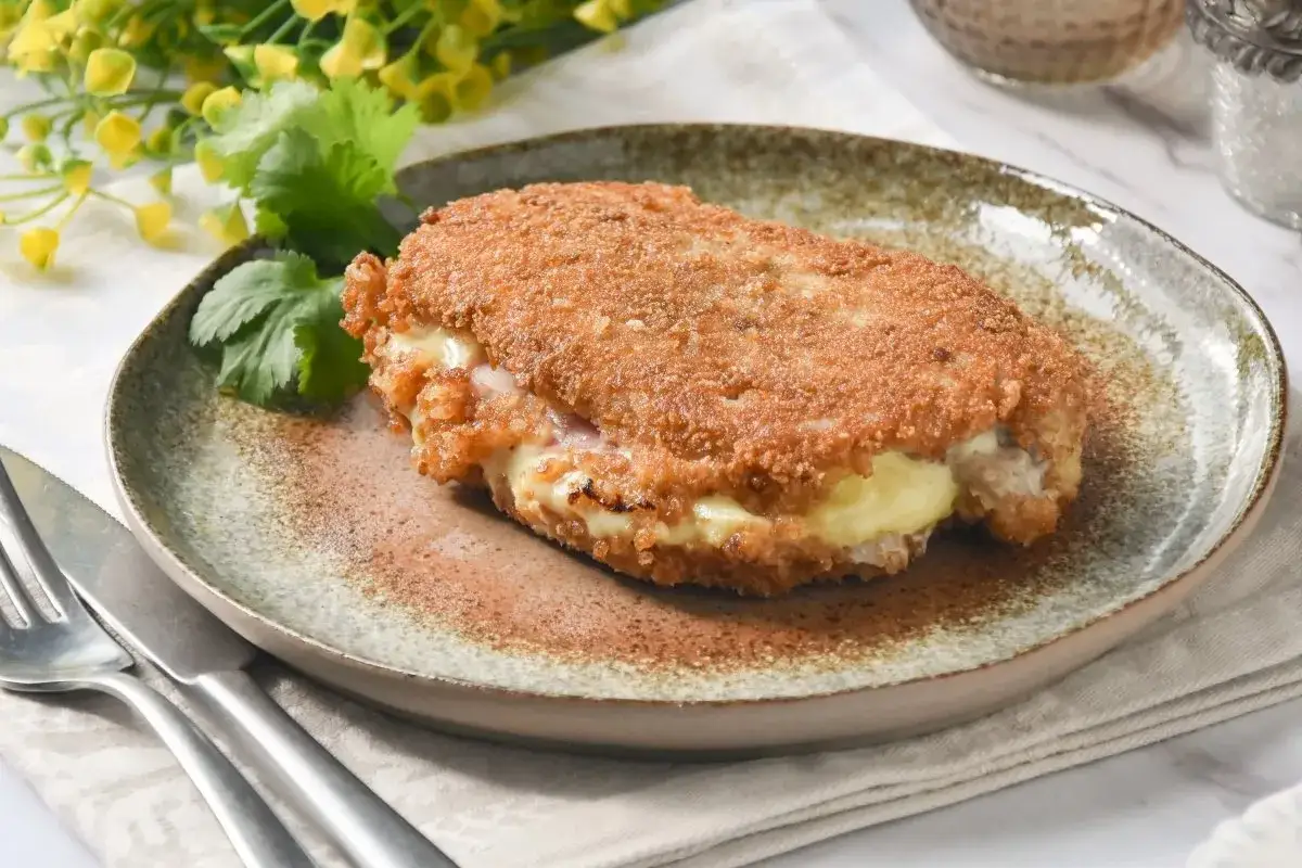 Deliciosos libritos de lomo empanados, rellenos de queso fundido y jam&oacute;n, servidos en un plato r&uacute;stico con cilantro y flores amarillas.