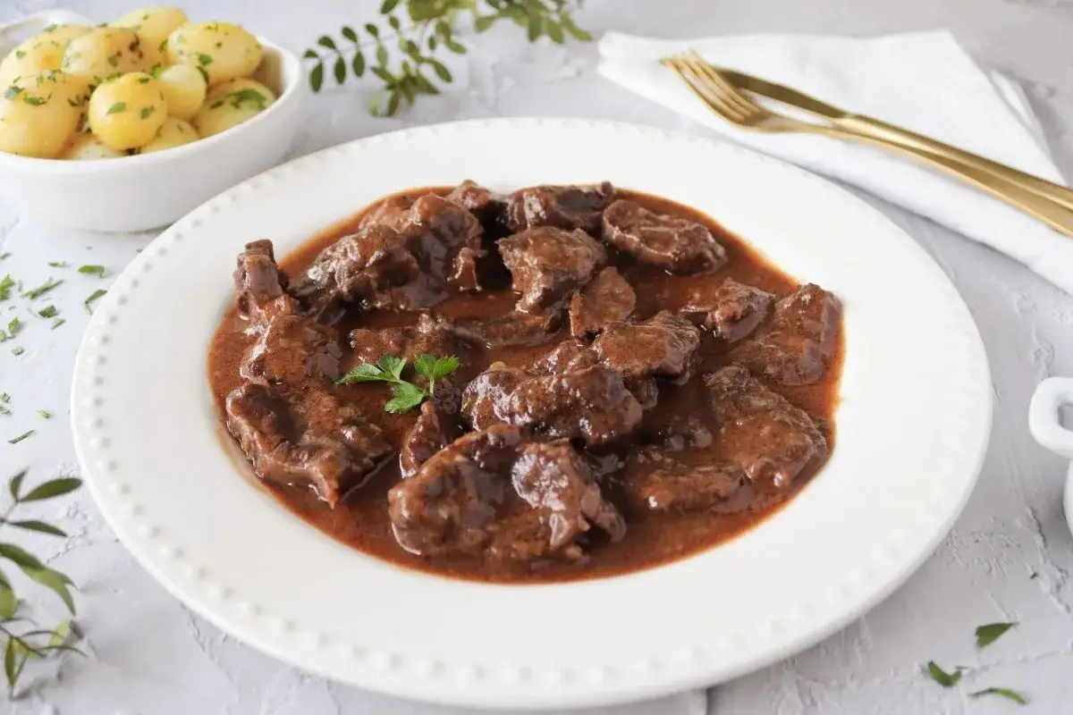 Sabroso morcillo de ternera estofado en salsa, servido en plato blanco con patatas cocidas y perejil picado.