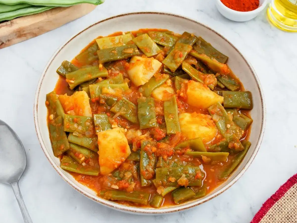 Un plato de jud&iacute;as verdes con jam&oacute;n y patatas en salsa de tomate. Un guiso casero lleno de sabor.