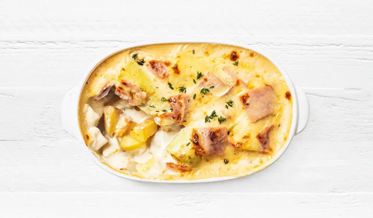 Grat&eacute;n cremoso de patatas y puerros al horno, con trozos de jam&oacute;n y hierbas arom&aacute;ticas.