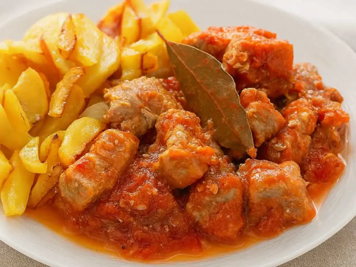 Carne con tomate receta: trozos de carne guisada en salsa de tomate, servida con patatas fritas doradas.