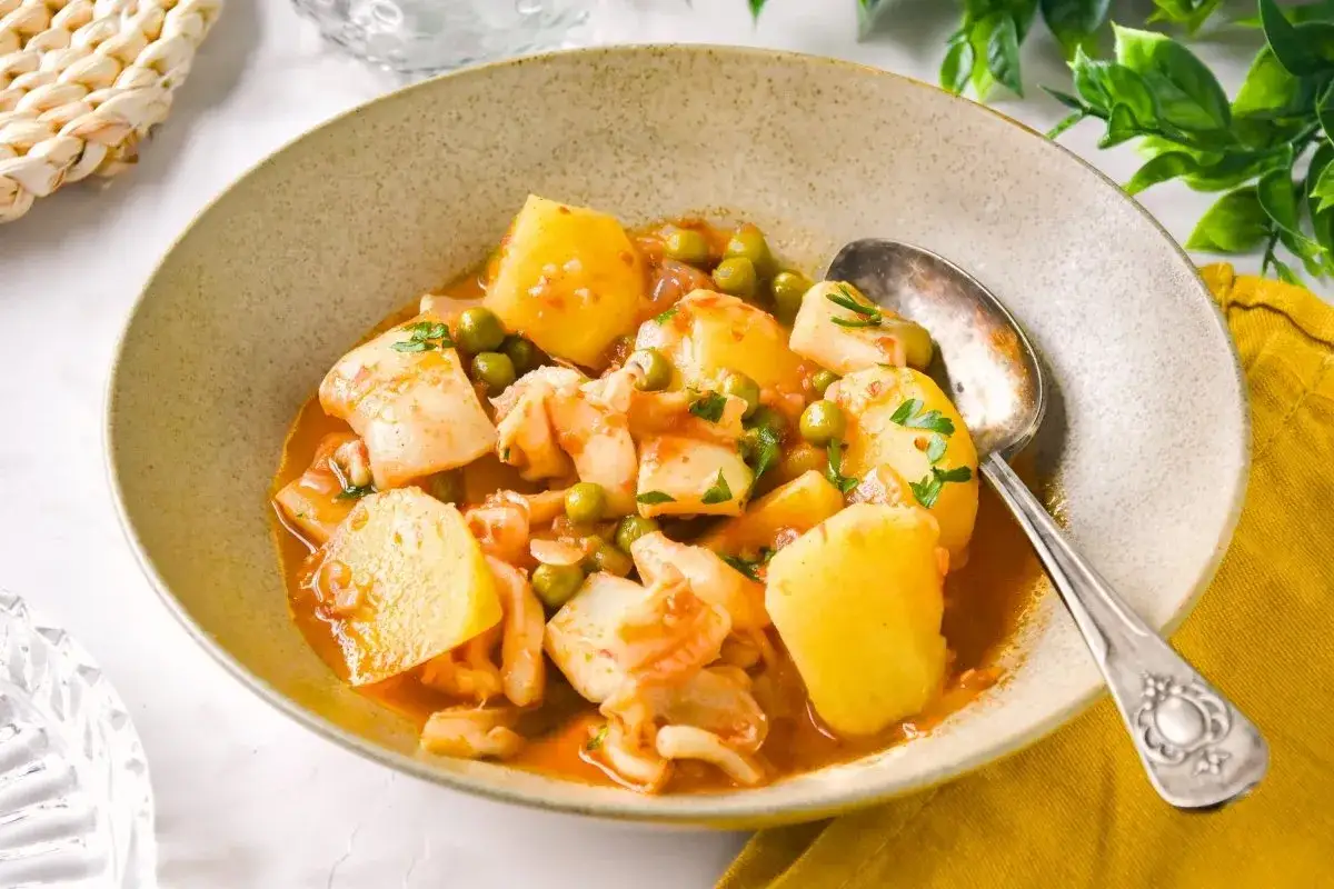 Un plato humeante de sepia con patatas, guisantes y perejil picado en una cazuela de barro.