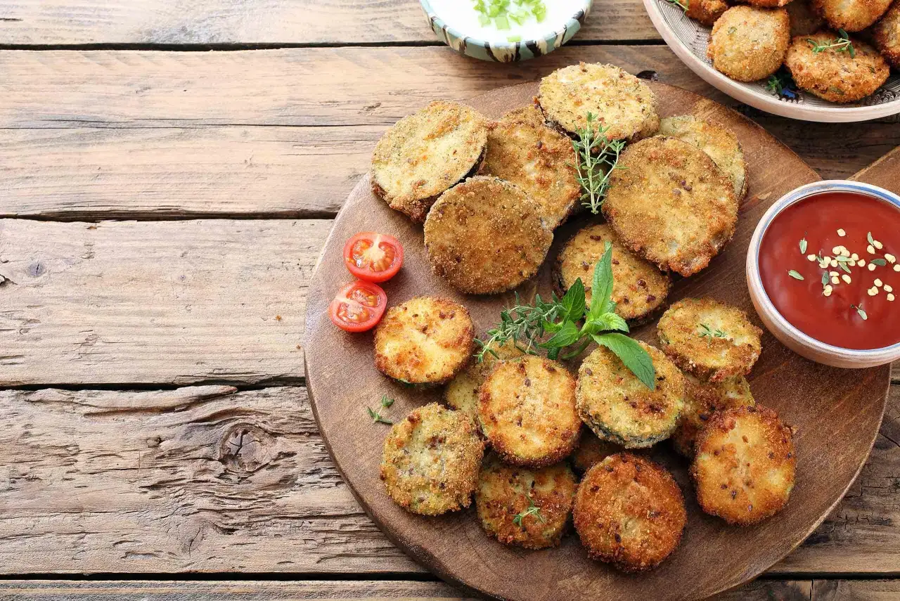 Berenjenas rebozadas con harina y huevo, doradas y crujientes, servidas con tomates y salsa.