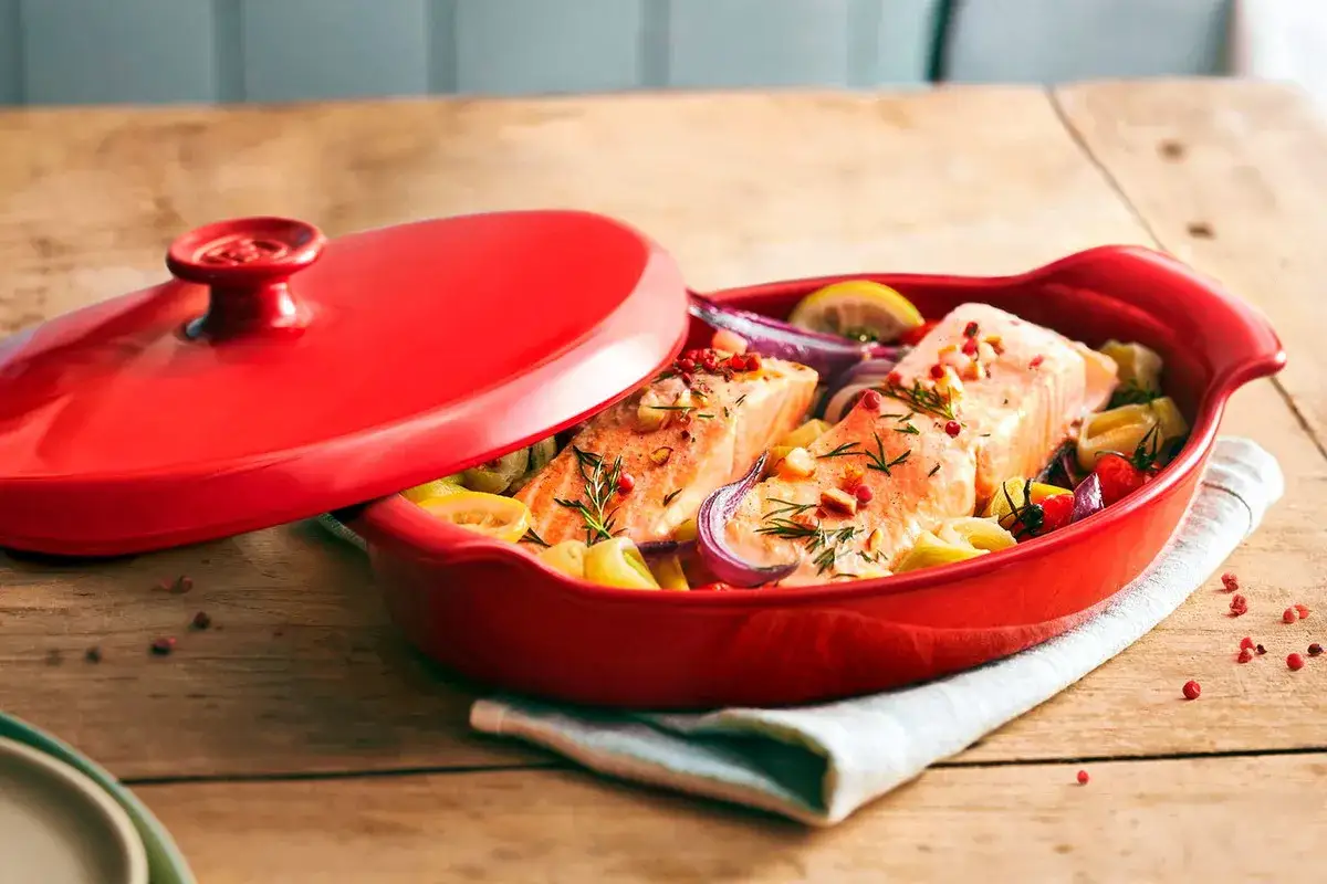 Dos filetes de salmón en papillote con verduras y limón en una cazuela roja.