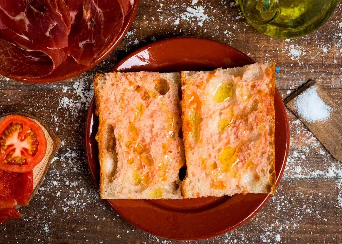 Dos rebanadas de pan r&uacute;stico con tomate rallado y aceite de oliva, listas para disfrutar como pa amb tom&agrave;quet. Acompa&ntilde;ado de jam&oacute;n serrano y sal.