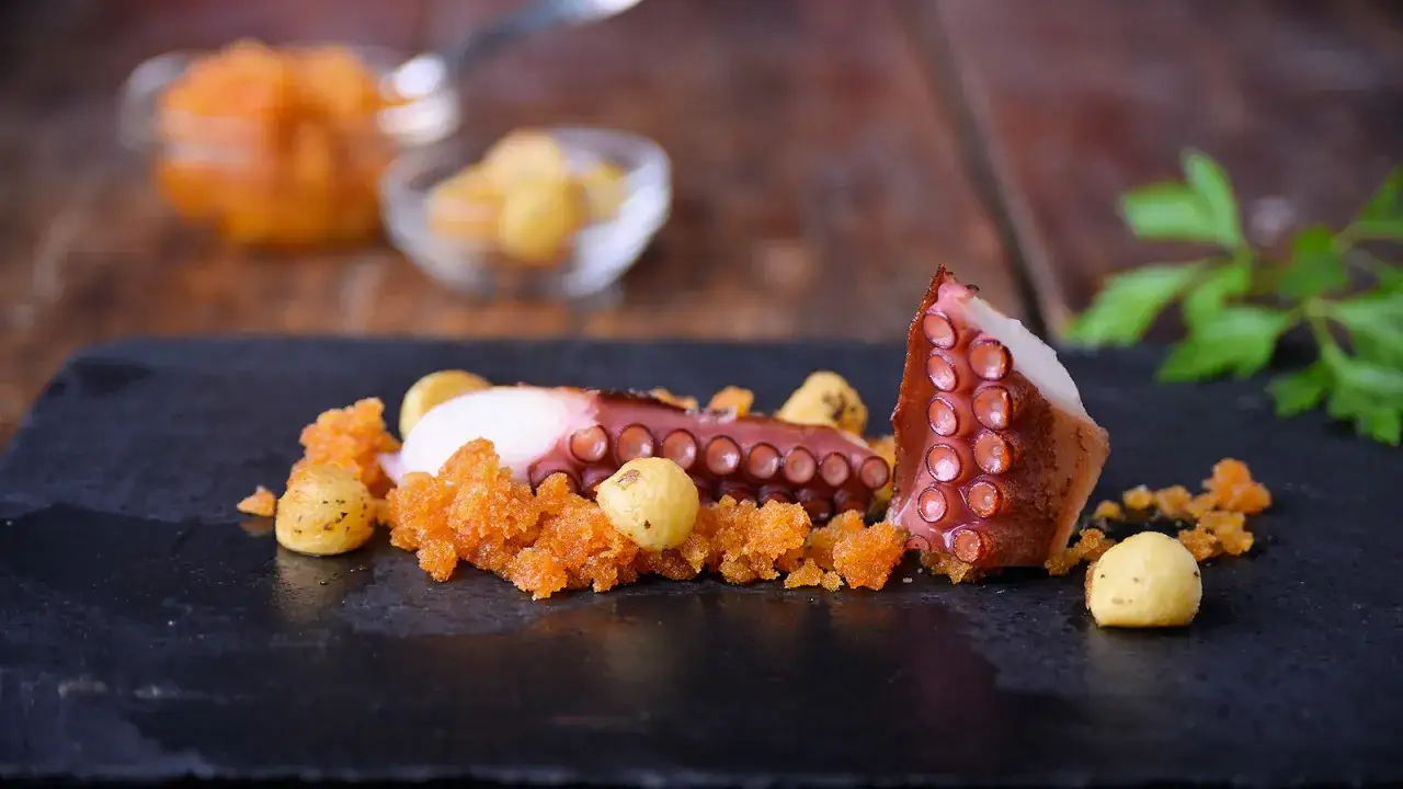 Pulpo tierno con patatas crujientes y un toque de piment&oacute;n, servido sobre pizarra negra.