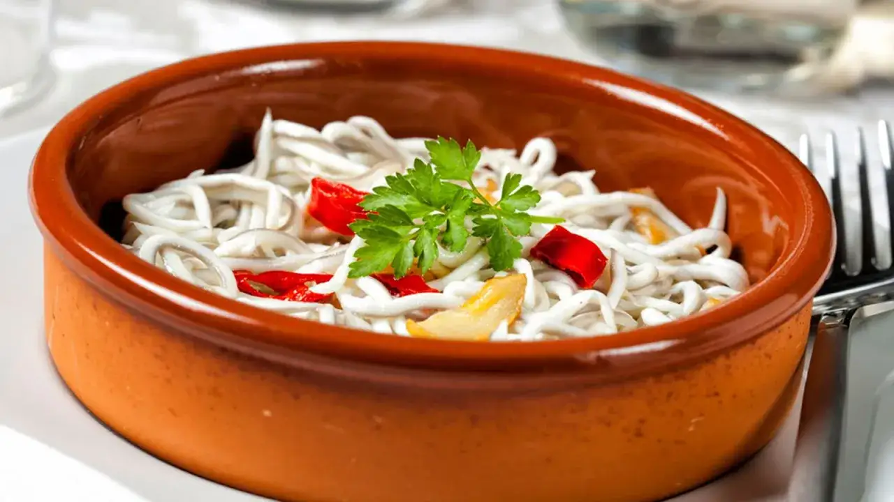 Delicioso revuelto de gulas con trocitos de pimiento rojo y perejil fresco, servido en una cazuela de barro.