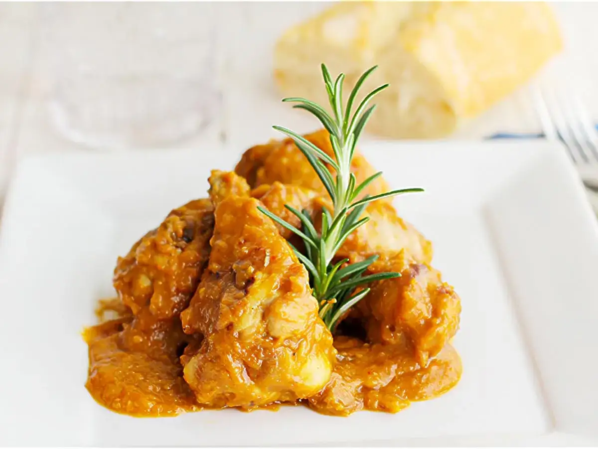 Sabroso pollo con almendras en una salsa dorada, adornado con romero fresco. Un plato que evoca tradición y sabor.