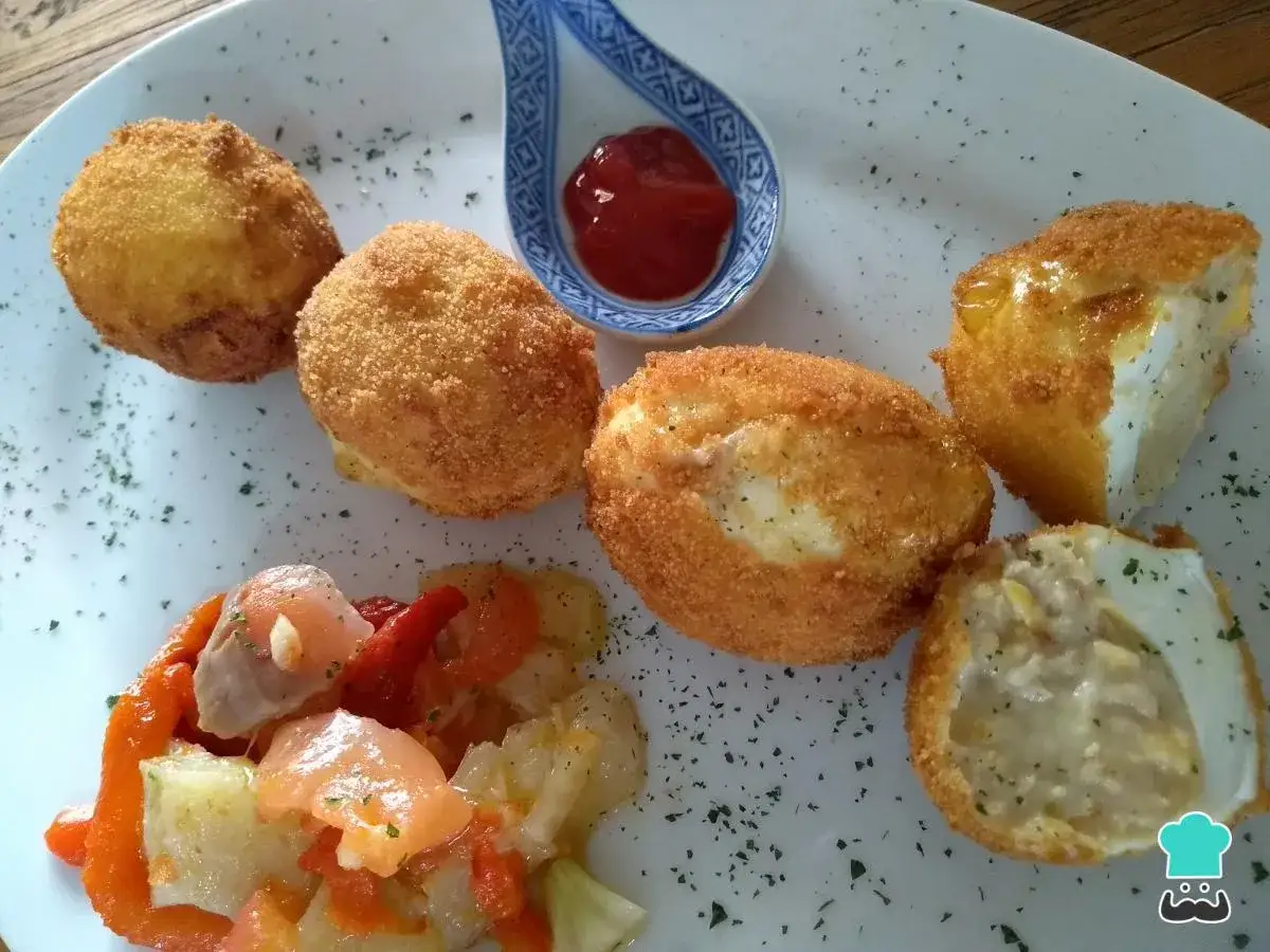 Huevos rebozados rellenos de bechamel, servidos con pimientos asados y una pizca de perejil.