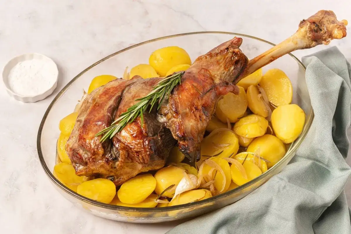 Pierna de cordero al horno con patatas doradas, ajo y romero. Un plato jugoso y arom&aacute;tico listo para servir.