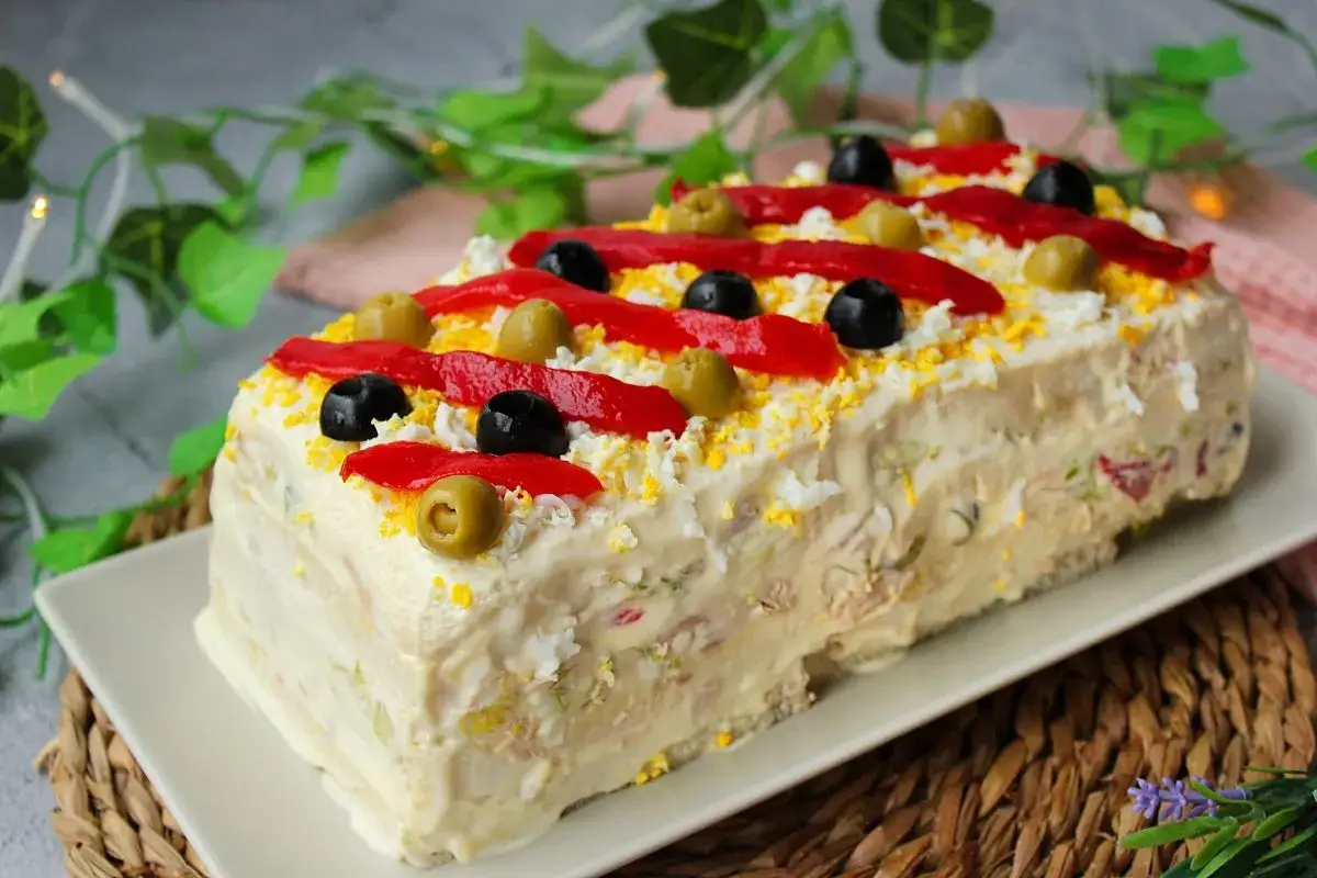 Pastel de at&uacute;n decorado con pimientos rojos, aceitunas negras y verdes, y huevo rallado. &iexcl;Una delicia para compartir!