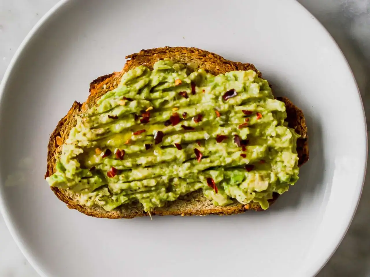 Tostada de pan integral con aguacate machacado, aceite de oliva y hojuelas de chile rojo. Una idea sencilla para recetas con aguacate.