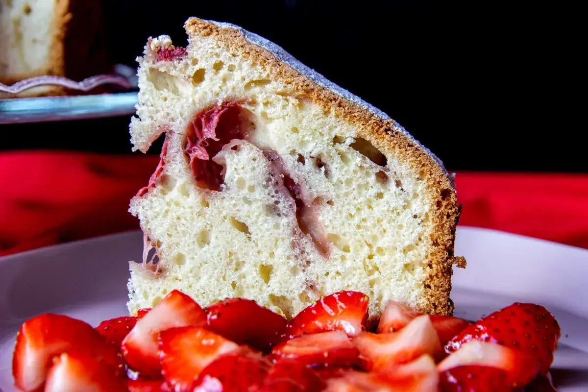Rebanada de bizcocho de fresa esponjoso con trozos de fruta y fresas frescas cortadas en primer plano.