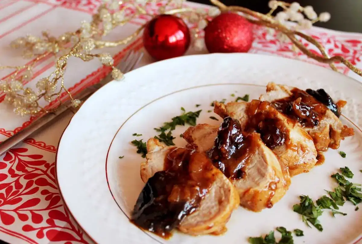 Delicioso solomillo de cerdo al Pedro Ximénez, servido en un plato blanco con perejil picado. Decoración festiva con adornos navideños.