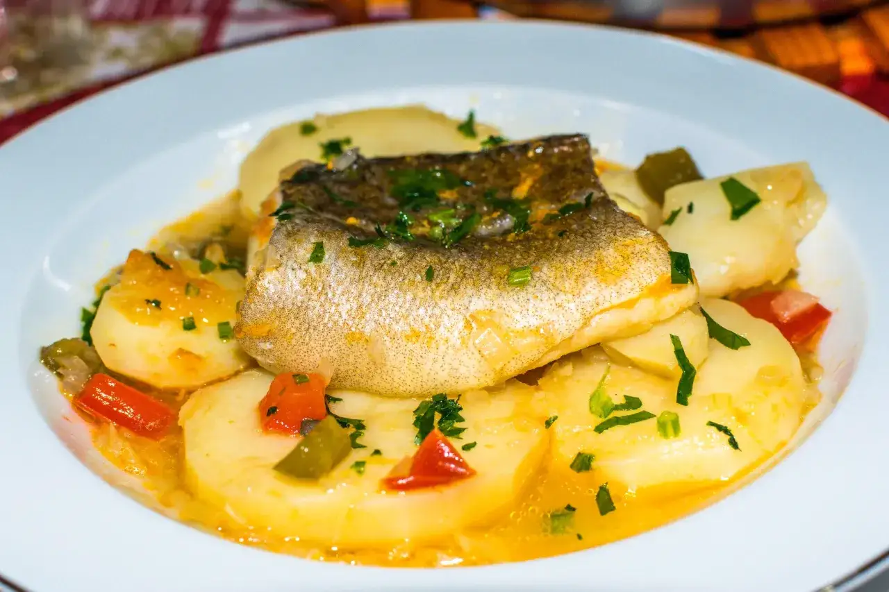 Un filete de pescado sobre patatas cocidas con pimientos y perejil. Un plato delicioso de patatas con bacalao.