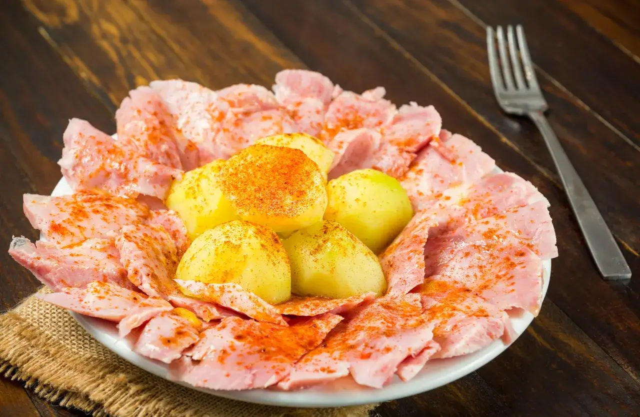 Plato de lacon con cachelos, patatas cocidas espolvoreadas con piment&oacute;n y lonchas de jam&oacute;n.