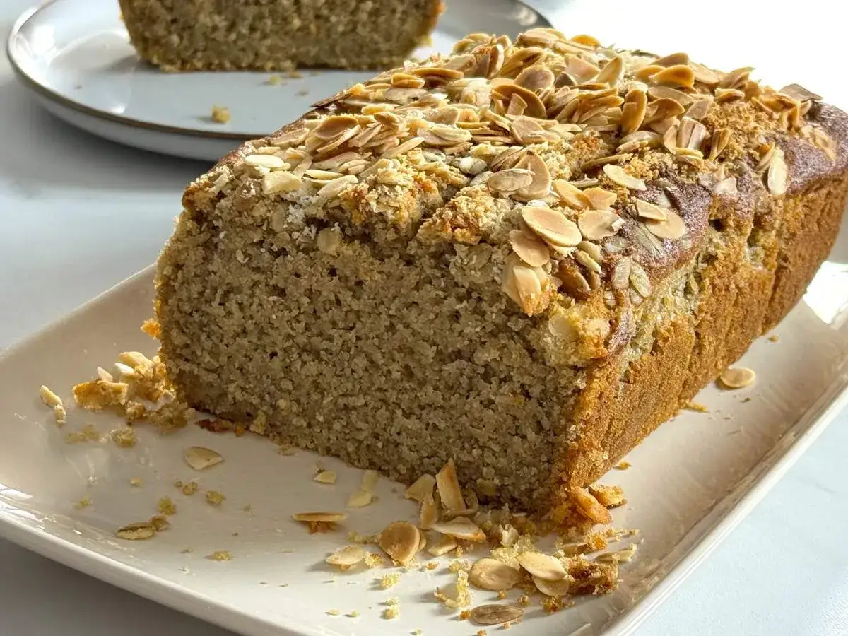 Un delicioso bizcocho de avena, cubierto con almendras laminadas, servido en una bandeja blanca.