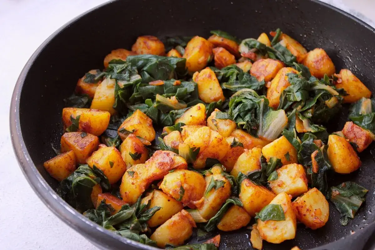 Un plato casero de acelgas con patatas doradas, reci&eacute;n hecho en una sart&eacute;n.