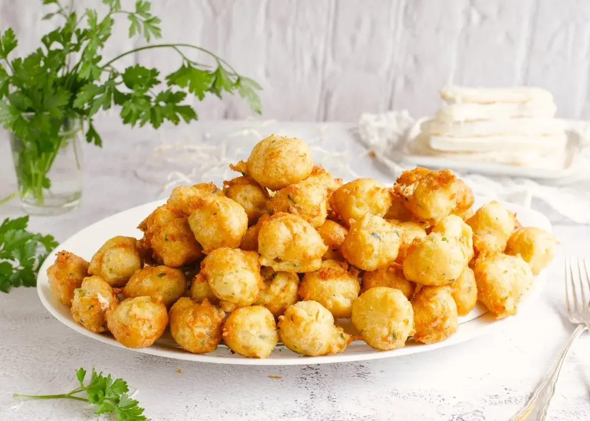 Mont&oacute;n de bu&ntilde;uelos de bacalao dorados y esponjosos, servidos en un plato blanco, con perejil fresco al lado.