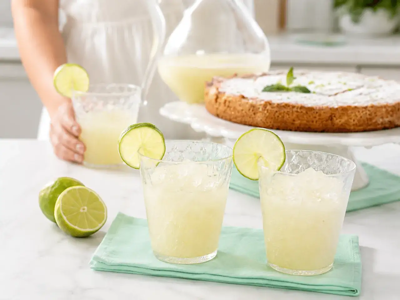 Dos vasos de granizado de lim&oacute;n refrescante, decorados con rodajas de lima, junto a limones frescos y un pastel.