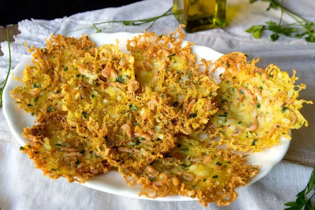Tortillas de camar&oacute;n crujientes y doradas, con peque&ntilde;os camarones y perejil picado, servidas en un plato blanco.